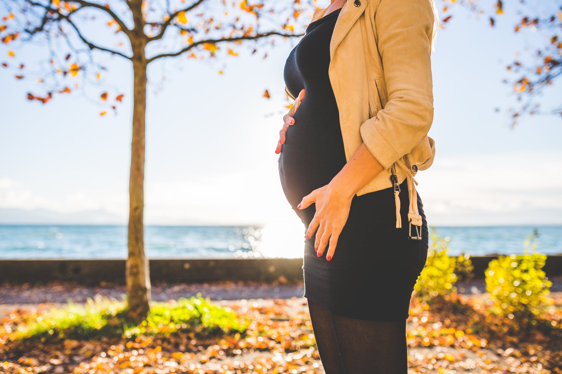 pregnant woman wearing beige long sleeve shirt standing near brown tree at daytime