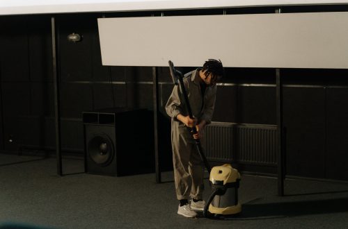 a man holding a vacuum cleaner near a speaker