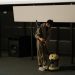 a man holding a vacuum cleaner near a speaker