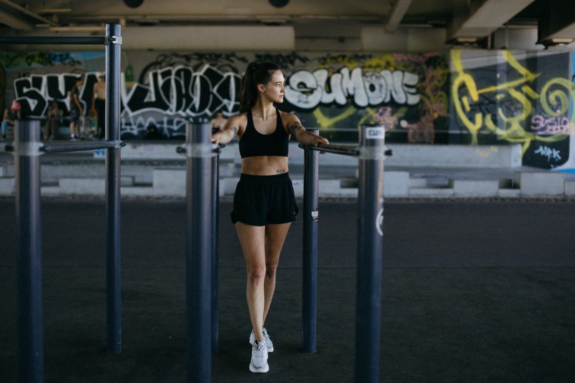 woman in black sports bra and black shorts holding on l parallel bars