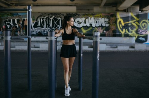 woman in black sports bra and black shorts holding on l parallel bars